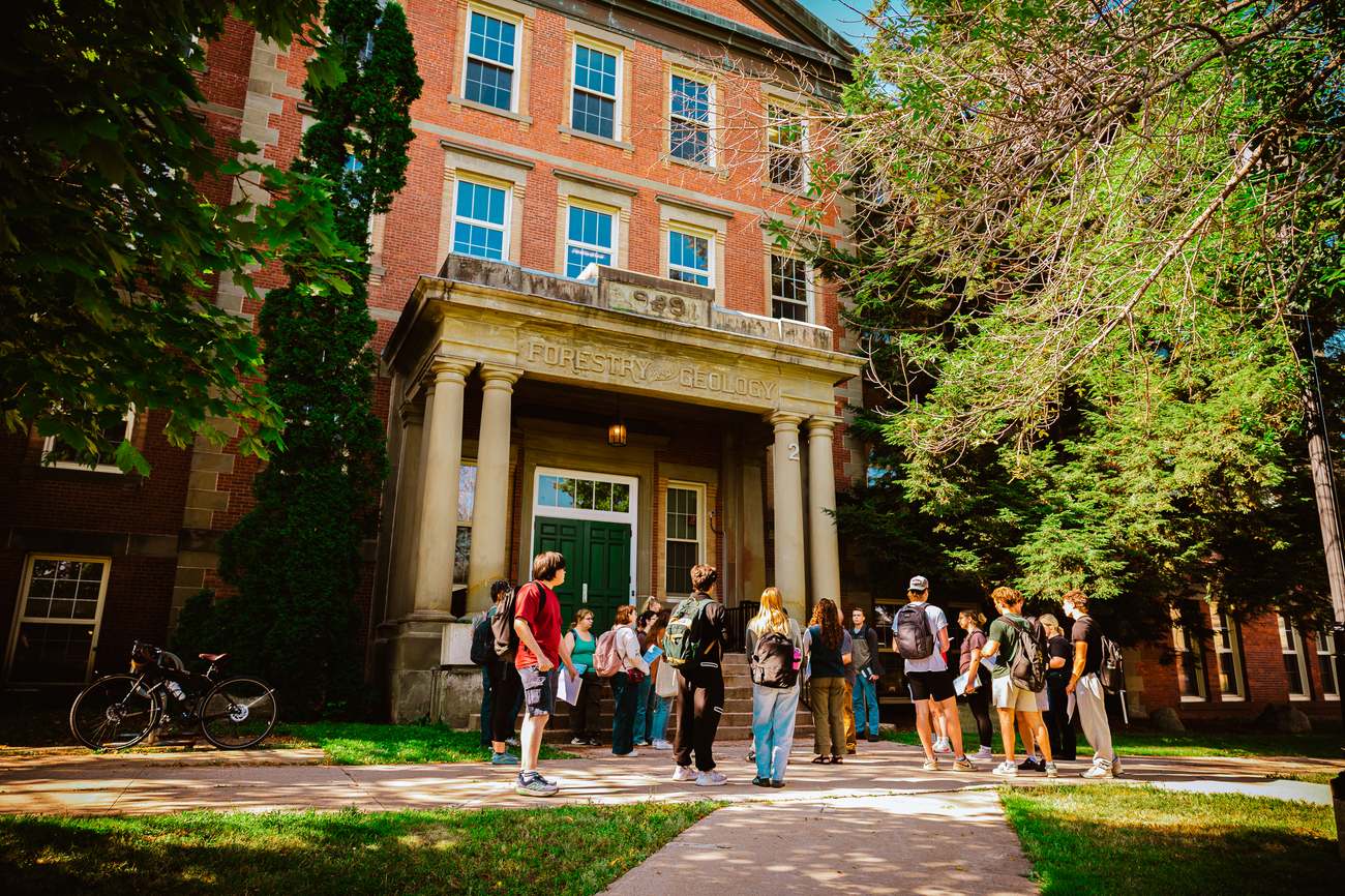 A ForEM class gathered with their instructor in front of UNB's historic Forestry and Geology building, its name carved above the entrance